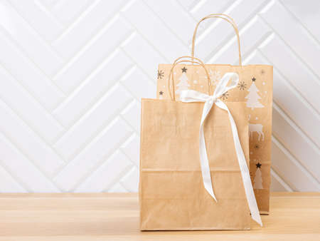 Blank paper carrier bag with handles for shopping, facing front on right side of a wood veneer table with white wall background providing copy space to left.の写真素材