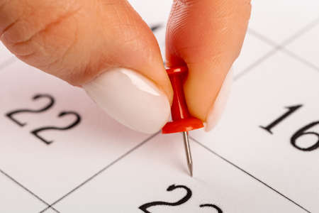 red Hand pin stuck on the day of the month in the calendar, business concept. beautiful female hand...