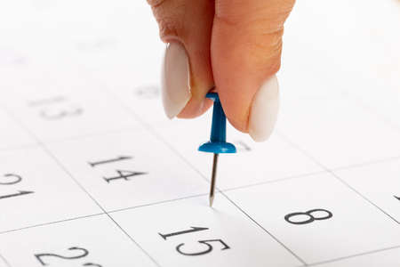 beautiful female Hand with manicure pushes a blue pin on a calendar day 15の写真素材