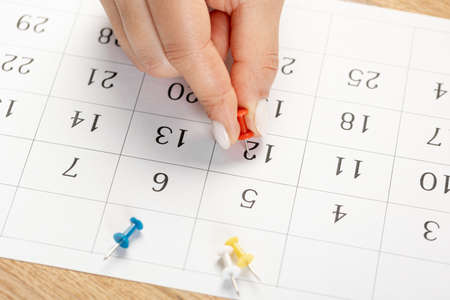 red Hand pin stuck on the day of the month in the calendar, business concept. beautiful female hand...