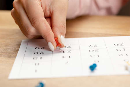red Hand pin stuck on the day of the month in the calendar, business concept. beautiful female hand fingersの写真素材
