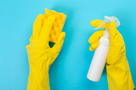 The hands of a housewife in yellow rubber protective gloves hold a bottle of household chemicals and...