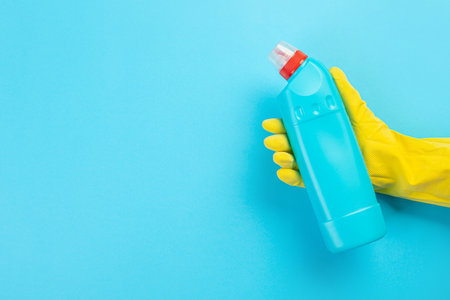 A hand in a rubber glove holds a green bottle of detergent on a blue background. Banner with copy...