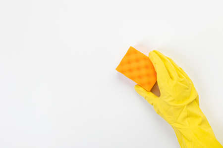 The hand of a housewife in a yellow protective rubber glove holds a sponge for cleaning agent on a...