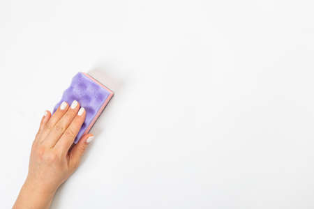 Housewife's hand holds a sponge for cleaning agent on a gray background. Detergent for various surfaces in the kitchen, bathroom and other rooms.の写真素材