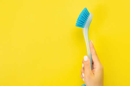 The housewife's hand holds a cleaning brush. Empty space for text or logo on a yellow background. Early spring or regular cleaning. Cleaning and cleaning concept.の写真素材