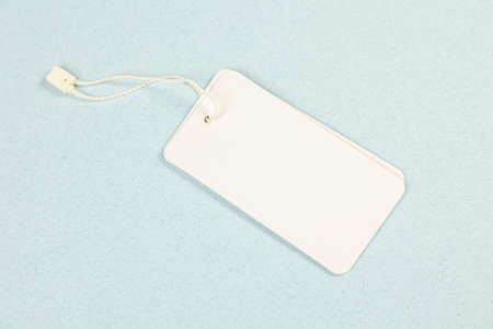 An empty white price tag lies on a gray-blue background with a soft shadow.