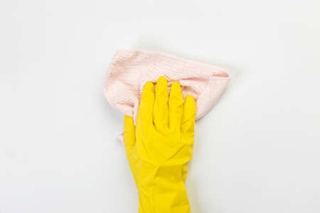 The hand of a housewife in a yellow protective rubber glove holds a rag with microfiber fiber for cleaning agent on a gray background. Detergent for various surfaces in the kitchen, bathroom and other rooms.の写真素材
