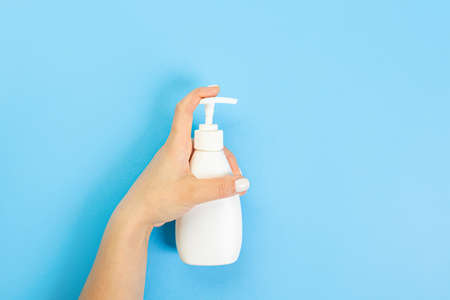 Housewife's hand holds a spray with cleaning agent on a blue background. Detergent for various surfaces in the kitchen, bathroom and other rooms. close-up. Light pastel blue background.の写真素材