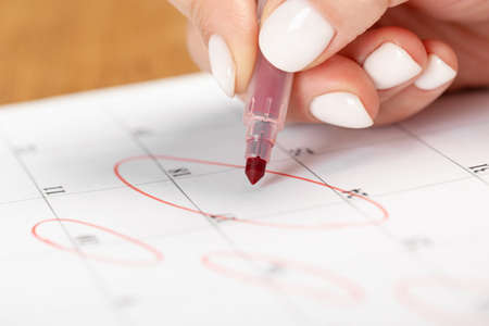 female hand marking with a red pen on a calendar circles the day, deadline concept