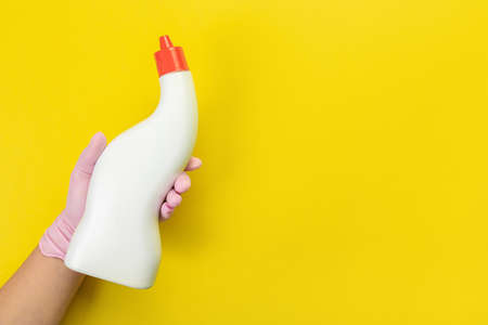Close up of female hand in pink gloves holds bottle with cleaner liquid for washing dishes with place for text on yellow background. Cleaning supplies concept. copy spaceの写真素材