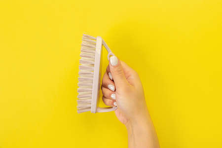 The housewife's hand holds a cleaning brush. Empty space for text or logo on a yellow background....