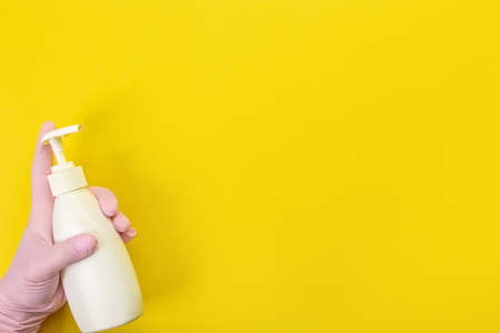 Close up of female hand in pink gloves holds bottle with cleaner liquid for washing dishes with place for text on yellow background. Cleaning supplies concept. copy spaceの写真素材