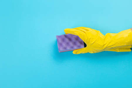 worker's hand in a yellow rubber protective glove with a purple sponge or dishwashing. A maid or housewife takes care of the house. general or regular cleaning.の写真素材