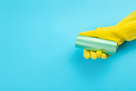 A hand in a yellow glove holds a plastic disposable trash bag on a blue background. place with copy space.の写真素材