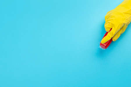 A hand in a yellow glove holds a plastic cleaning brush on a blue background. Banner with copy...