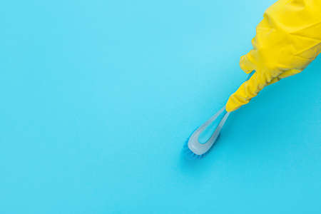 A hand in a yellow glove holds a plastic cleaning brush on a blue background. Banner with copy space. Chemical cleaners, household chemicals, brushes and collage supplies.の写真素材
