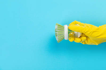 A hand in a yellow glove holds a plastic cleaning brush on a blue background. Banner with copy space. Chemical cleaners, household chemicals, brushes and collage supplies.の写真素材