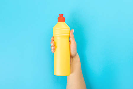 Housewife's hand holds a spray with cleaning agent on a blue background. Detergent for various surfaces in the kitchen, bathroom and other rooms. close-up. Light pastel blue background.の写真素材