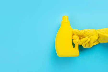 A hand in a rubber glove holds a yellow bottle of detergent on a blue background. Banner with copy...