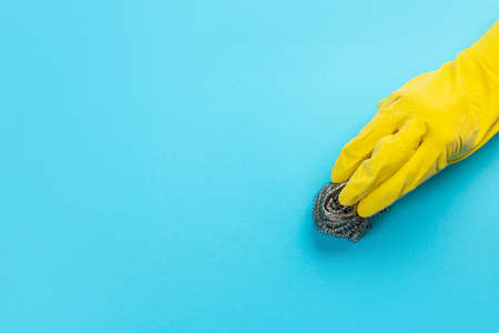 A hand in a yellow glove holds a plastic cleaning brush on a blue background. Banner with copy space. Chemical cleaners, household chemicals, brushes and collage supplies.の写真素材