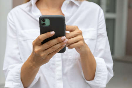 female hands hold a modern mobile phone on the street. news, education, modern app, shopping order, work onlineの写真素材