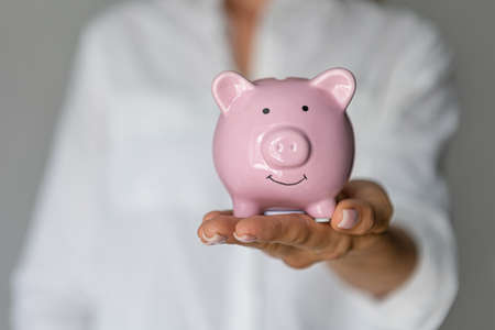 female hands holding pink piggy bank indoors investment accumulation crisisの写真素材