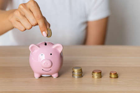 Close-up of a woman's hands putting a euro coin in a piggy bank, saving money as an investment in times of crisis and inflationの写真素材