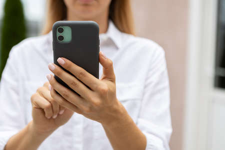 female hands hold a modern mobile phone on the street. news, education, modern app, shopping order, work onlineの写真素材
