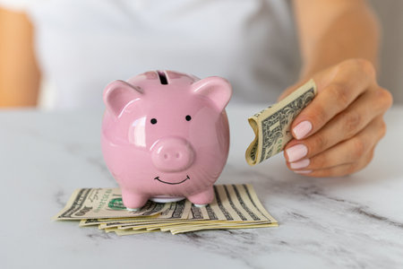 Close-up of a woman's hands put dollar paper money in a piggy bank, next to a calculator on the table.saving money in a crisis and inflationの写真素材