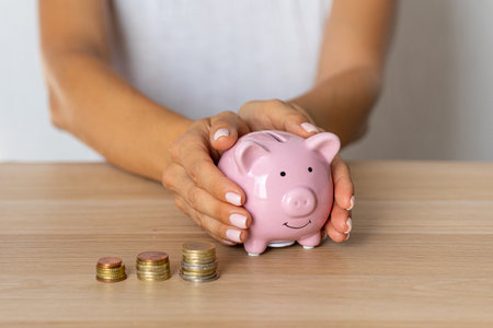 Close-up of a woman's hands putting a euro coin in a piggy bank, saving money as an investment in times of crisis and inflationの写真素材