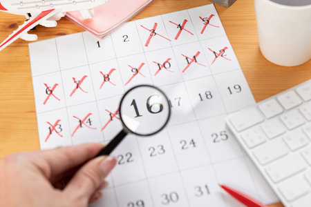 a hand with a magnifying glass examines the calendar and reminders for work from home online. glider on desktop with mouse and pen, keyboard. mark important plans in a diary at the office desk. 2023 calendar reminder concept.の写真素材