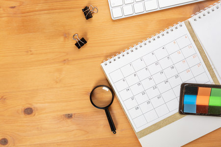 Calendar and reminders with magnifying glass, work from home online. glider on desktop with mouse and pen, keyboard. mark a holiday trip or plans in a diary at the office desk. 2023 calendar reminder concept.の写真素材