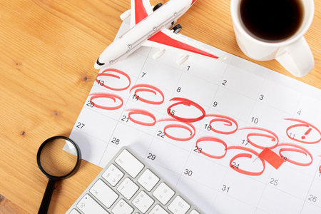 Calendar and reminders for work trips, travel and vacations. glider on desktop with airplane and magnifying glass and pen, keyboard. marking important dates and days in a diary at the office desk. 2023 calendar reminder concept.の写真素材