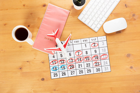 Calendar and reminders for business trip, travel and vacation. planner with airplane model on desktop with keyboard, mouse, coffee and succulent. marking important dates and days in a diary at the office desk. Reminder conceptの写真素材