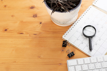 Calendar and reminders with magnifying glass, work from home online. glider on desktop with mouse and pen, keyboard. mark a holiday trip or plans in a diary at the office desk. 2023 calendar reminder concept.の写真素材