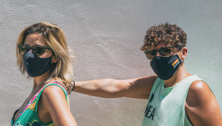 Two friends looking at each other wearing a protective mask. Two female friends face to face with a protective face mask standing in front of a wall on a city sidewalkの写真素材