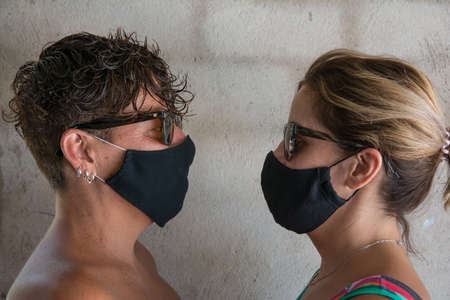 Two friends looking at each other wearing a protective mask. Two female friends face to face with a protective face mask standing in front of a wall on a city sidewalkの写真素材