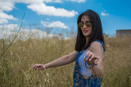 Woman touching the grass with her hand walking in a field. Woman walking alone through the field. Individual outdoor activities. Lifestyle in natureの写真素材