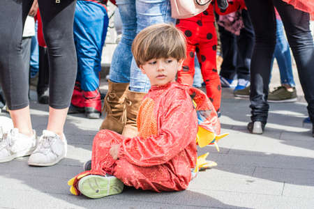 Boy In Dinosaur Costume Sitting On The Ground Surrounded By People. A little boy prepares for Halloween.の写真素材