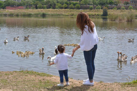 Mother and little girl enjoying in the park. Mother and her daughter enjoying a beautiful day in the field and watching the ducks in the river. Family and mother's day concept.の写真素材
