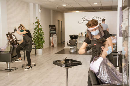 Hairdressers adapt to new security measures to prevent coronavirus. COVID 19. Hairdressers wear protective screens and sanitary masks. Badajoz, Spainのeditorial素材