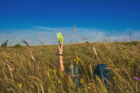 Woman With A Sanitary Mask After The Coronavirus Outbreak In Spain. Adult Woman Lying Down In The Field Holding A Sanitary Mask In Her Hands And Enjoying Nature. Covid 19. Lifestyle.の写真素材