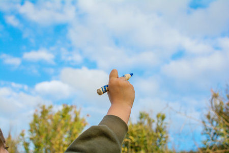 A Child's Hand With A Blue Pencil Painting The Sky. Creative Photography With Copy Spaceの写真素材