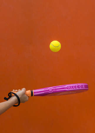 Hand Holding A Paddle Tennis Racket Hitting The Ball On An Orange Background.Sports