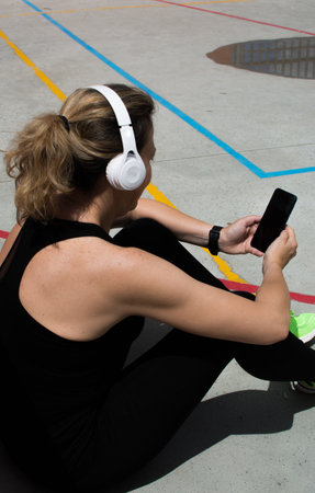 Sportsman With His Smartphone. Portrait Of A Sportswoman Sitting On An Urban Court And Using Her Smartphone. She Wears Headphonesの写真素材