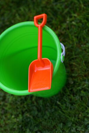 A vertical colour photograph of a child's green pail with an orange shovel, sitting on the grass.の写真素材