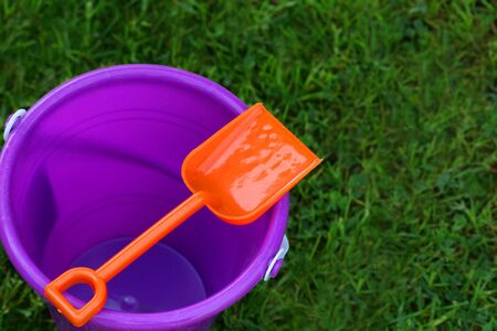 A horizontal colour photograph of a child's purple pail with an orange shovel, sitting on the grass.の写真素材