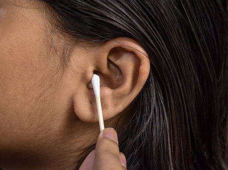 The woman carefully cleans her ear with an earbud, ensuring personal hygiene and maintaining ear...