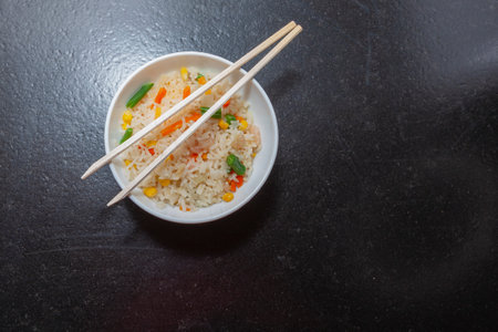 Three delicious Chinese rice with prawns, green beans, corn and carrots, served in a white bowl on which there are two chopsticks.の写真素材